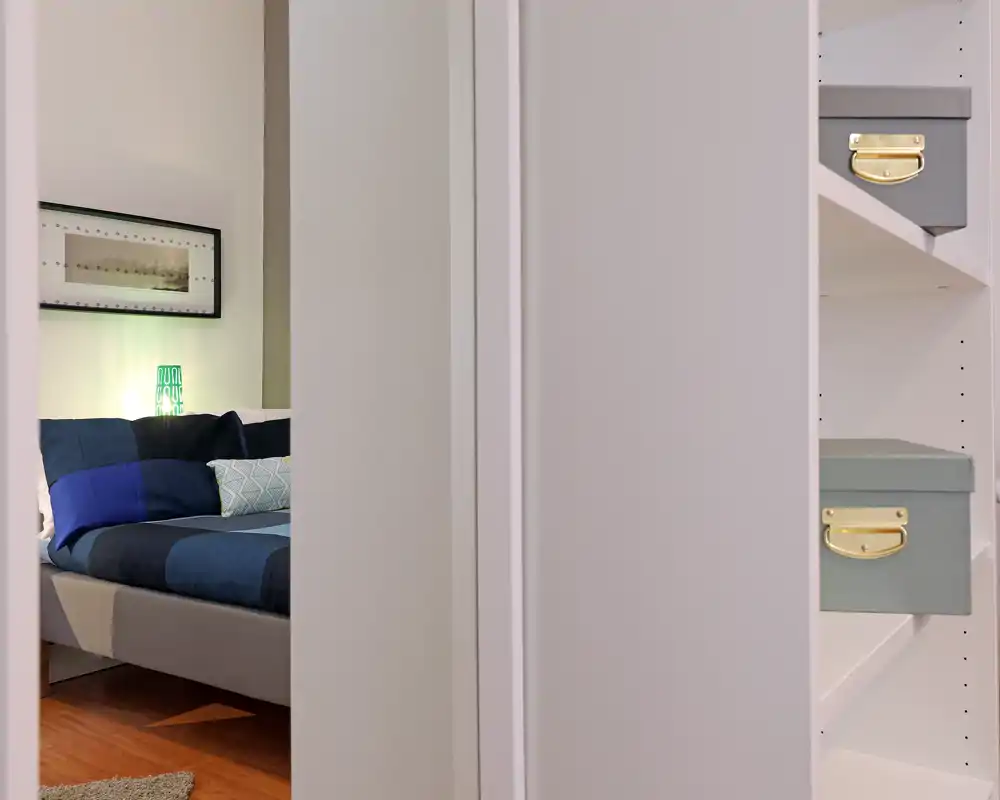 Camera da letto moderna e accogliente vista attraverso una porta, con letto ben rifatto, cuscini decorativi e una lampada da comodino che crea un'atmosfera calda.