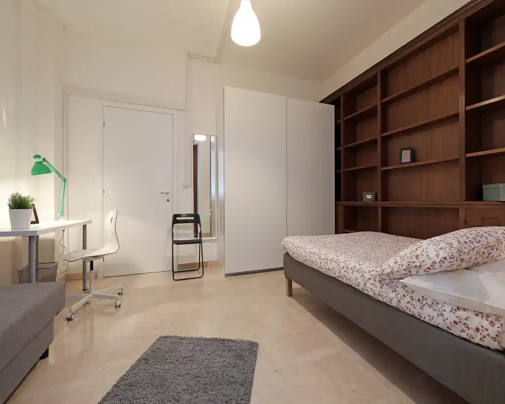 Camera da letto luminosa e ben allestita con letto matrimoniale, ampi scaffali, scrivania e armadio — perfetta per uno studente o professionista.