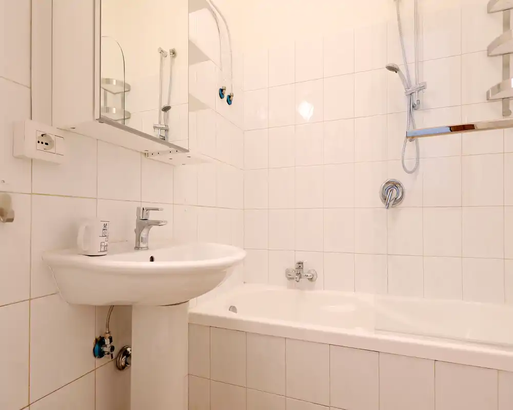 Bagno compatto e pulito con lavabo a colonna e vasca con doccia. Piastrelle bianche e rubinetterie cromate offrono un aspetto luminoso e neutro adatto agli annunci.