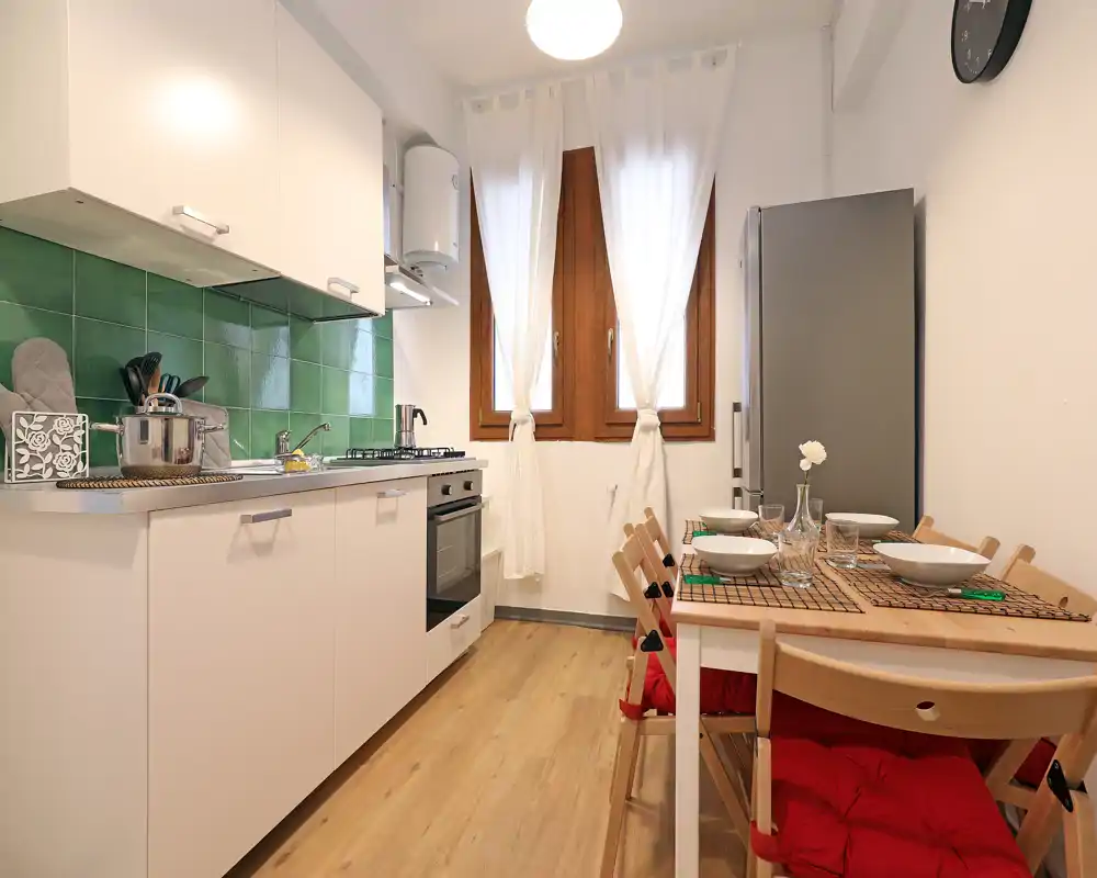 Cucina compatta e luminosa con mobili bianchi, paraschizzi verde, piano cottura a gas e un piccolo tavolo da pranzo per quattro persone — ideale per pasti accoglienti.