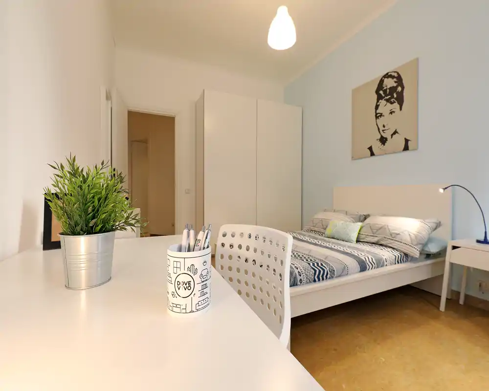 Dormitorio moderno y luminoso con cama doble con ropa de cama estampada, armario blanco y escritorio ordenado en primer plano; perfecto para una estancia confortable.