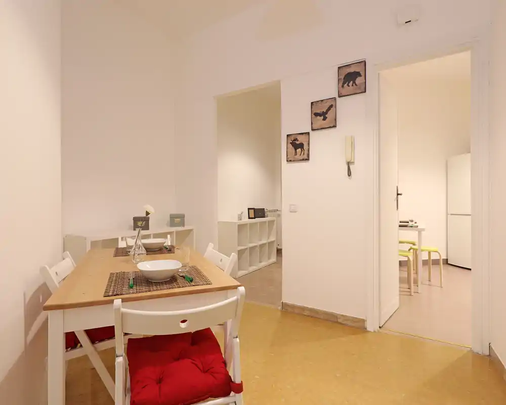 Área de comedor luminosa y ordenada con una mesa de madera para dos, sillas acolchadas y accesorios decorativos sencillos que crean un ambiente acogedor.