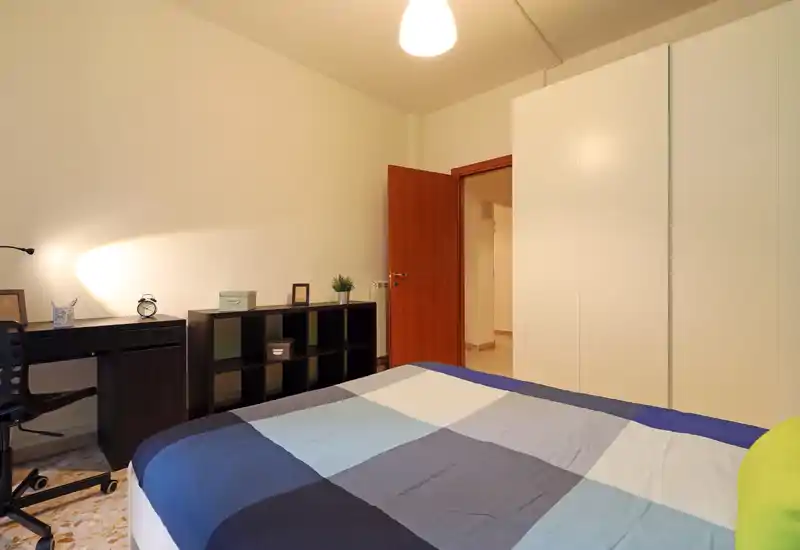 Dormitorio luminoso y de diseño sencillo con cama doble con edredón azul-gris, armario blanco, escritorio y estantería; perfecto para una estancia cómoda o para estudiantes.