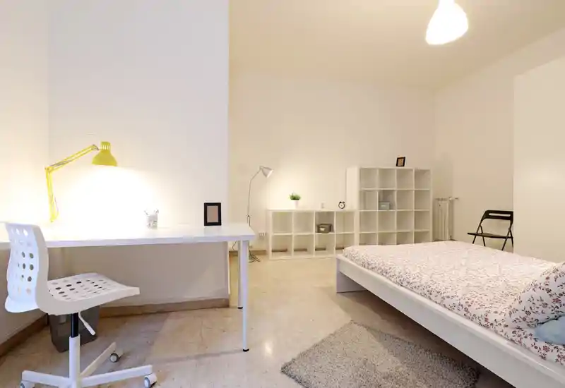 Dormitorio moderno y luminoso con cama plataforma blanca, edredón floral y un escritorio ordenado con lámpara — minimalista y bien iluminado.