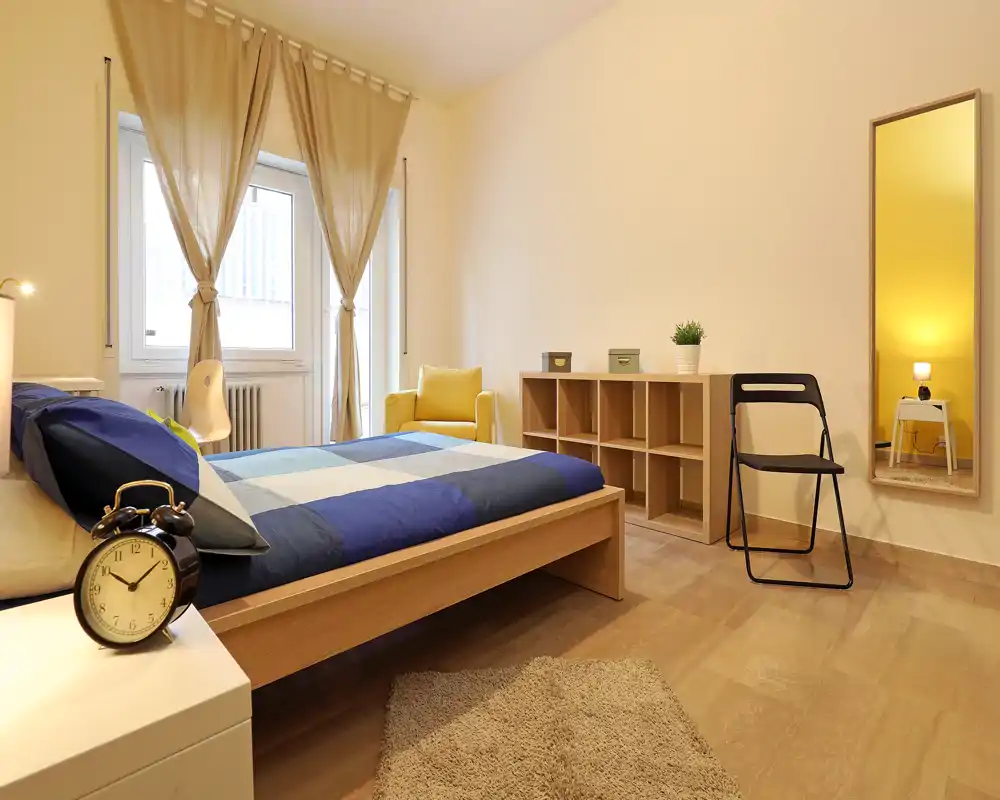 Chambre lumineuse et bien décorée avec un grand lit en bois, un tapis douillet et un fauteuil confortable près de la fenêtre. La lumière naturelle et les tons chauds créent une ambiance accueillante, idéale pour les annonces.