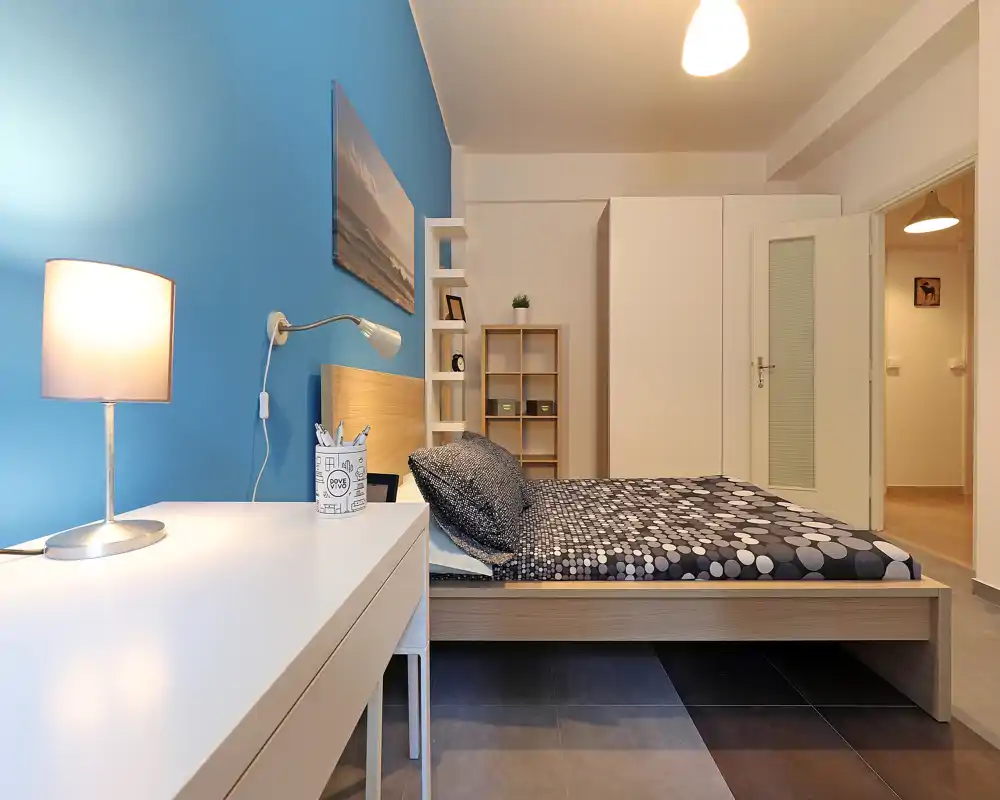 Bright, modern bedroom with a low wooden bed, patterned bedding, bedside lamp and a tidy desk — comfortable and well staged for short-term rental listings.