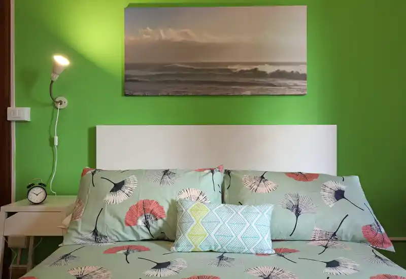 Chambre lumineuse et bien décorée avec un lit double à motif, coussins décoratifs et une photo de bord de mer au-dessus de la tête de lit ; idéale pour une annonce chaleureuse.