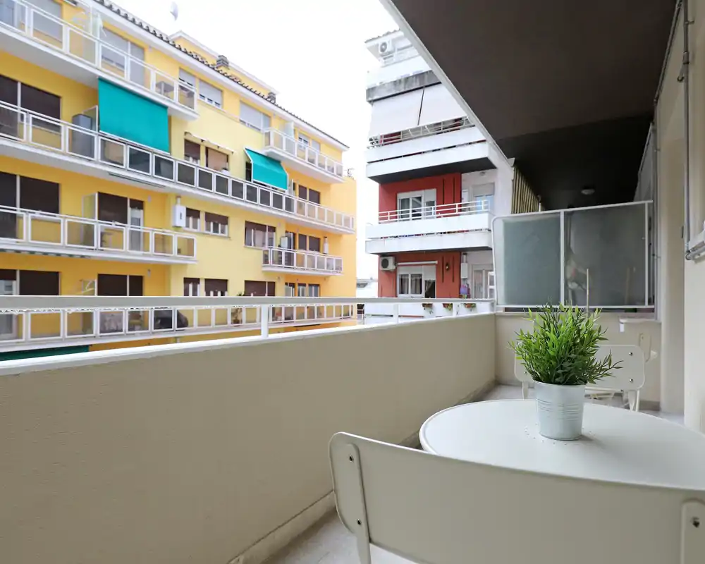 Balcone privato luminoso con piccolo tavolo rotondo e sedie, piacevole vista sulla città e pianta decorativa — ideale per il caffè mattutino.