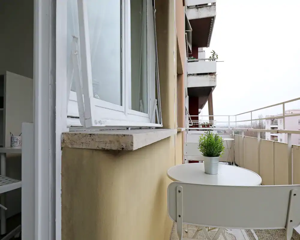 Balcón urbano compacto con mesa redonda pequeña y dos sillas, decorado con una planta en maceta — ideal para el café de la mañana y la vida exterior en poco espacio.