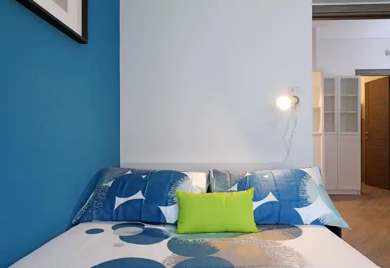 Bright, modern bedroom with blue accent wall, patterned bedding and a single bedside lamp — comfortable and well-styled for a rental listing.