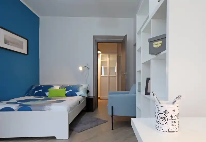 Bright, modern bedroom with a double bed against a blue accent wall, cozy textiles and tidy shelving — ideal for a stylish rental listing.