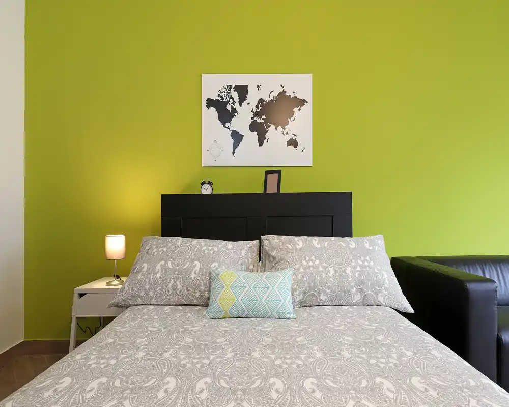 Chambre moderne et lumineuse avec literie à motifs, coussin décoratif et mur d'accent vert; lampe de chevet et tableau au-dessus de la tête de lit apportent style et chaleur.