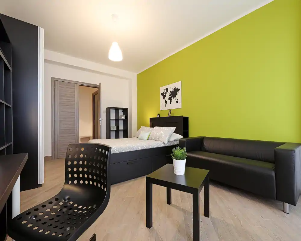 Chambre moderne et lumineuse avec lit double, canapé noir et mur vert accentué — un espace compact et bien décoré, idéal pour une personne ou un couple.