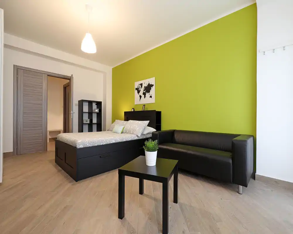 Chambre moderne avec lit plateforme noir et canapé assorti devant un mur vert vif ; décoration lumineuse et minimaliste avec une petite table et une plante.