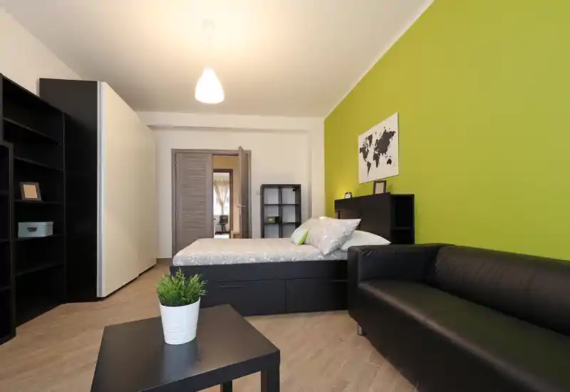 Chambre contemporaine avec lit double, meubles de rangement noirs et canapé noir confortable devant un mur vert; lumineuse, bien décorée et adaptée aux annonces.
