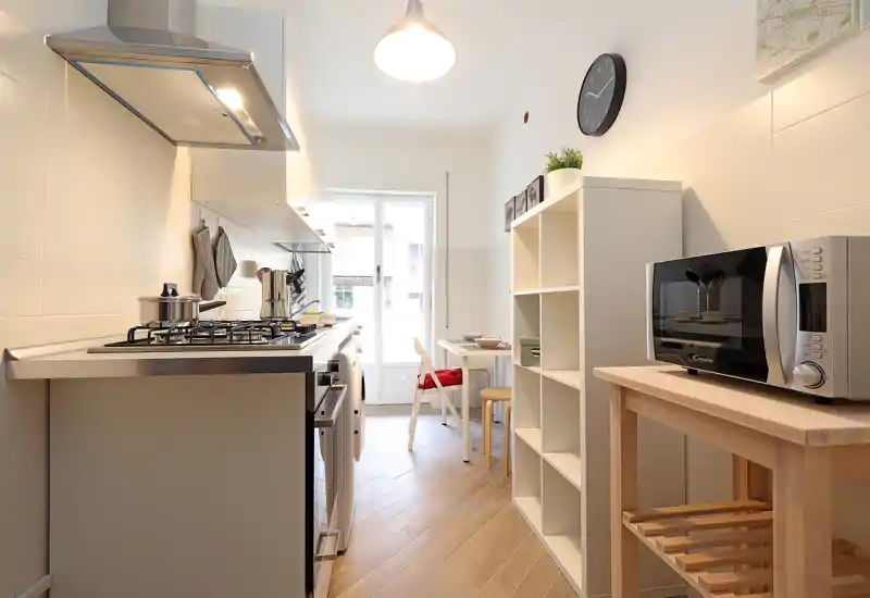 Bright, compact kitchen with a gas hob, microwave and a cozy breakfast nook by the window. Warm wooden floors and clean white cabinetry create a modern, inviting space.