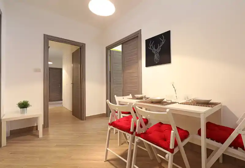 Bright, neatly staged dining area with a white table, red cushioned chairs and minimalist wall art — ideal for compact apartment listings.