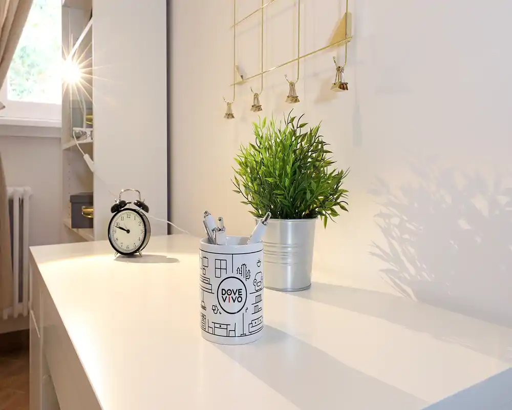Bright, minimalist desk corner with a potted plant, a decorative pen holder and an analog alarm clock; natural light adds warmth.