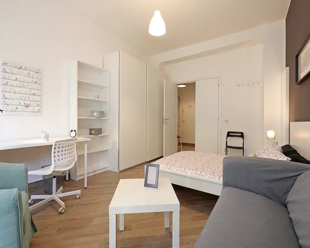 Dormitorio moderno y luminoso con cama doble, armario y zona de trabajo. Tonos neutros y textiles elegantes que crean un ambiente tranquilo y bien presentado.