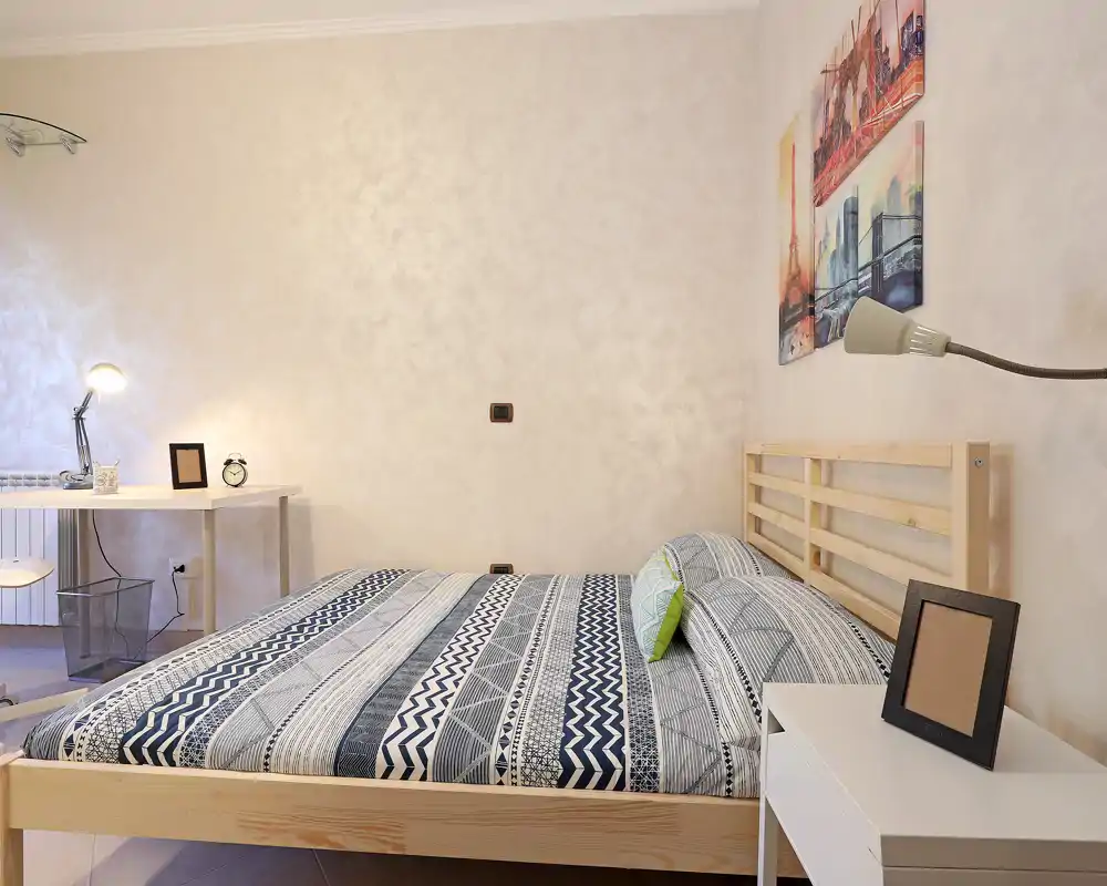 Dormitorio luminoso y moderno con cabecero de madera, edredón de estampado geométrico y mesita sencilla; decoración limpia y escritorio junto a la pared.