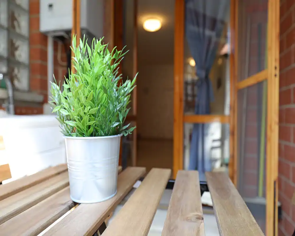 Detalle de balcón con una planta en maceta sobre una mesa de madera, fondo suave con la puerta y una cortina — un agradable espacio exterior privado.