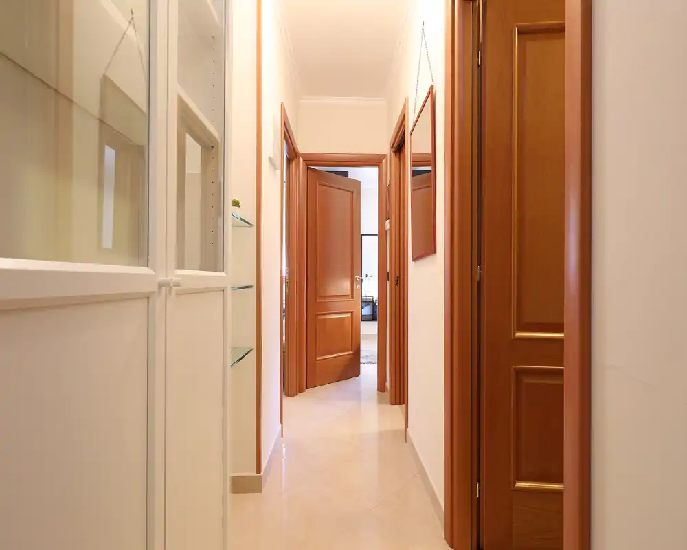 Pasillo de apartamento bien iluminado con suelo de baldosas brillantes, puertas de madera y armarios empotrados — recibidor ordenado y acogedor.