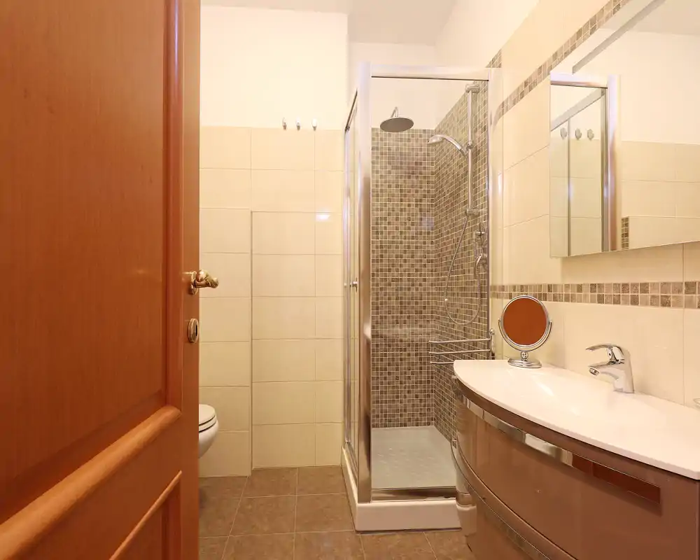 Baño moderno y luminoso con plato de ducha de vidrio, espejo con armario y mueble de lavabo curvo — limpio y bien iluminado.