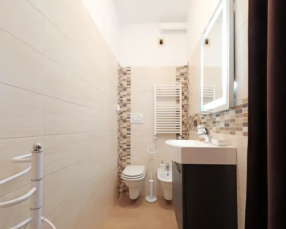 Baño moderno y compacto con inodoro suspendido, bidé, mueble lavabo con espejo iluminado y azulejos en tonos neutros — luminoso, limpio y funcional.