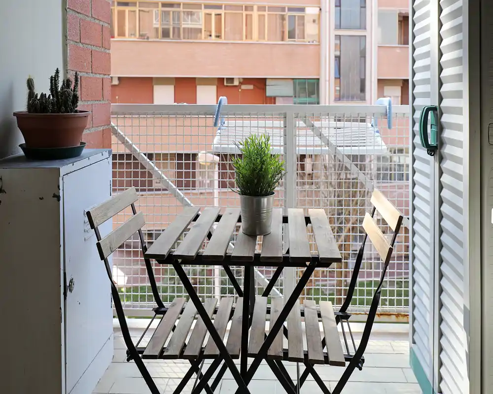 Balcón soleado con una pequeña mesa bistró de madera y dos sillas, decorado con una planta en maceta — ideal para el café de la mañana o para relajarse al aire libre.
