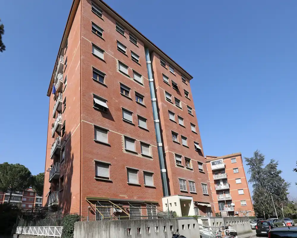 Vista exterior de un edificio residencial de varios pisos en ladrillo con cielo despejado, balcones y accesos en planta baja — adecuada para mostrar la fachada y la ubicación.