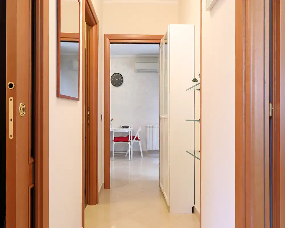 Recibidor/pasillo bien iluminado que conduce a la zona principal, con suelo de baldosa claro, marcos de madera y espejo en la pared.