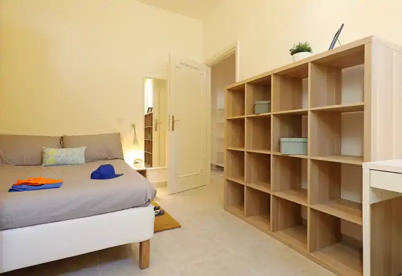 Bright, neatly staged bedroom with a comfortable double bed, soft pillows and a large open shelving unit that provides ample storage—ideal for rental photos and listing presentations.