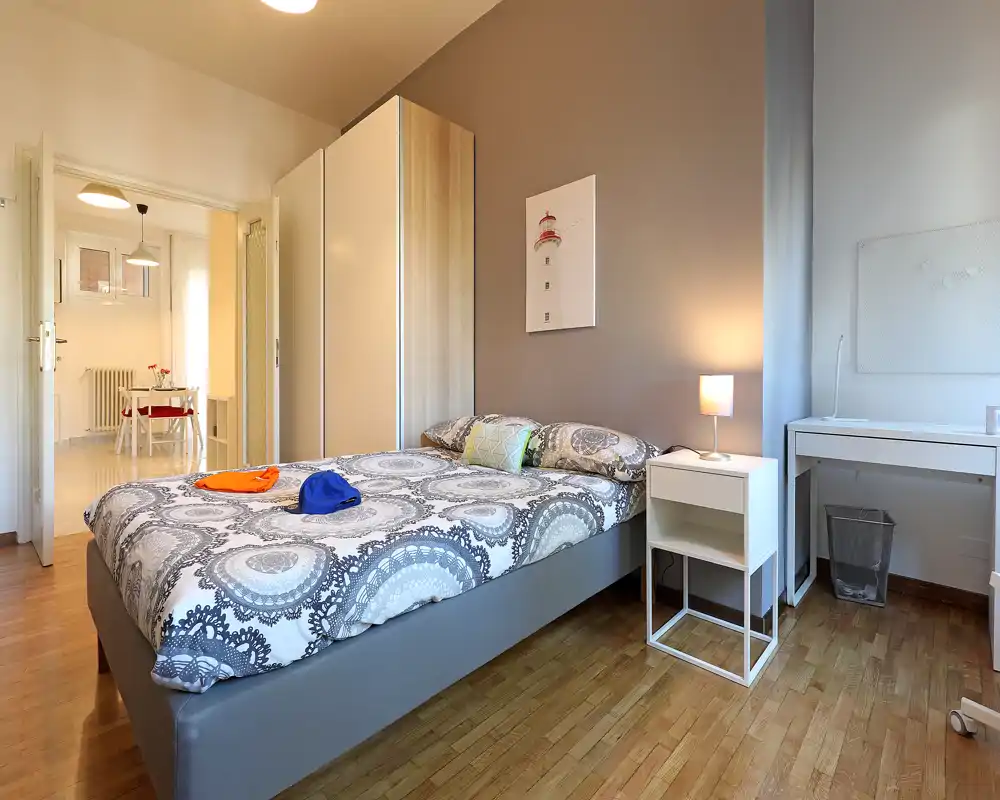 Dormitorio luminoso y bien presentado con cama doble, mesita y escritorio; tonos neutros y luz cálida crean un ambiente acogedor.