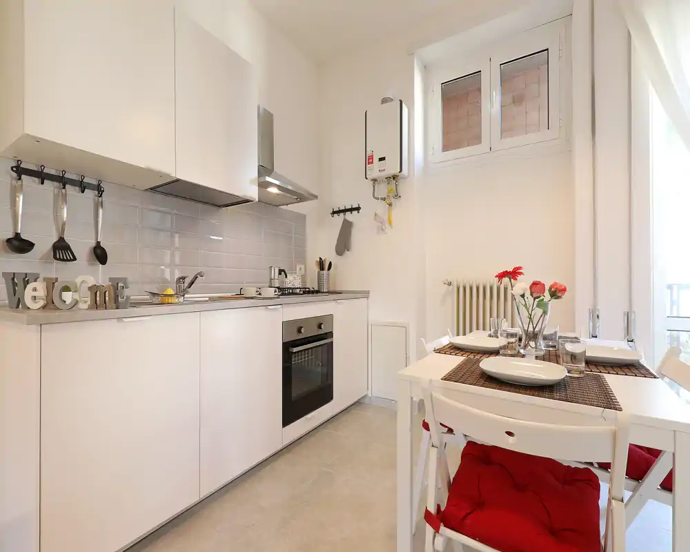 Bright modern kitchen with white cabinets, built-in oven and a small dining table set for four — well staged and welcoming for guests.