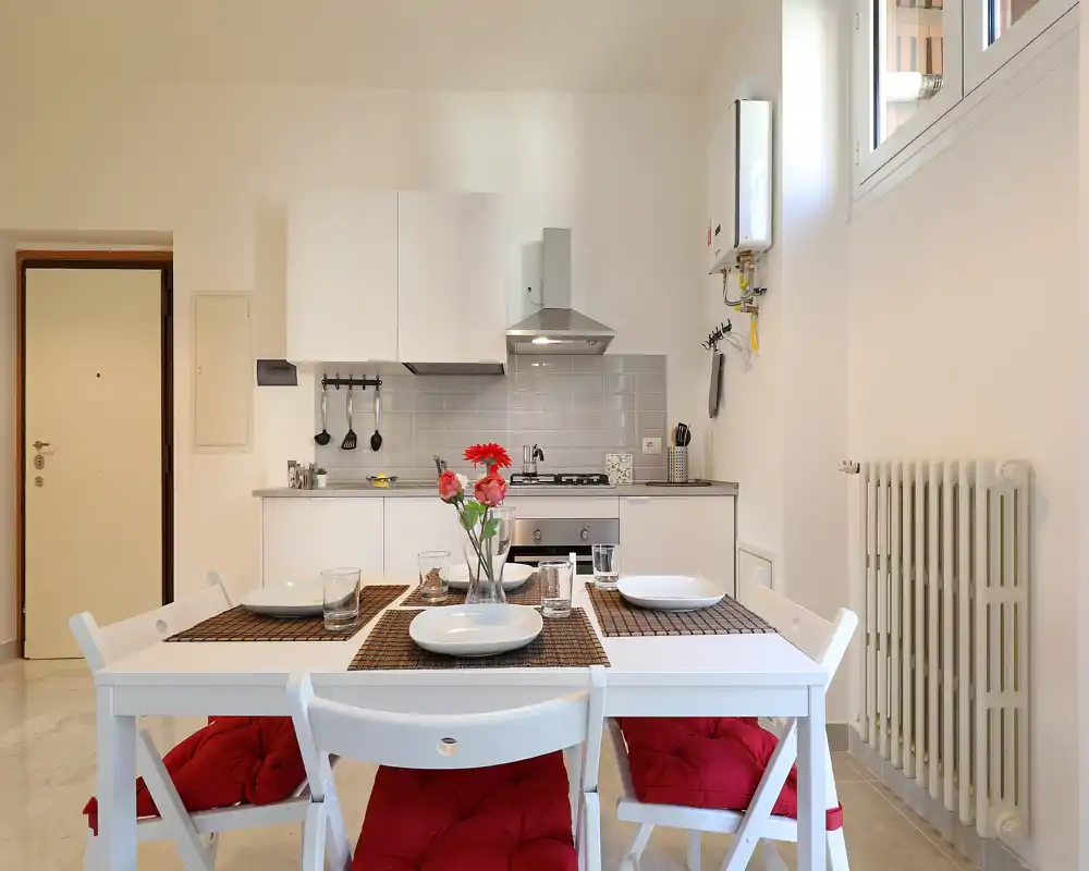 Bright, modern kitchenette with a dining table set for four. White cabinetry, stainless steel hood and a compact oven create a clean, functional space ideal for a small apartment.
