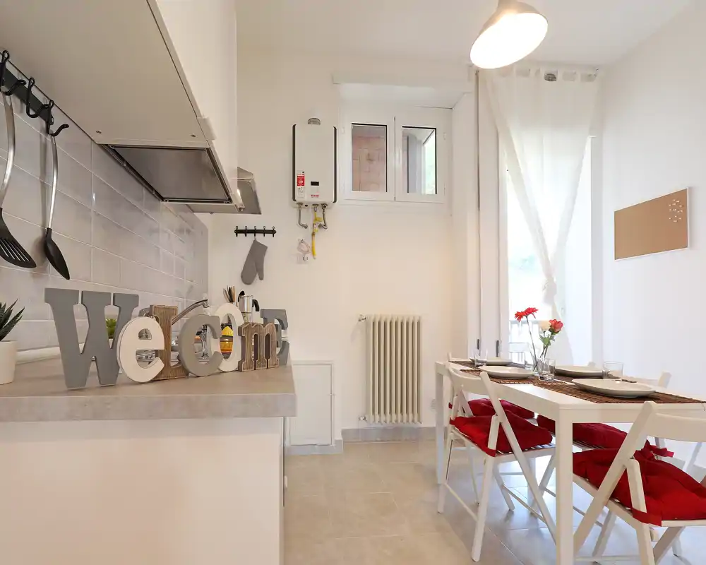 Bright, compact kitchen with a small dining table, decorative cushions and a welcoming counter display; ideal for a cozy apartment.