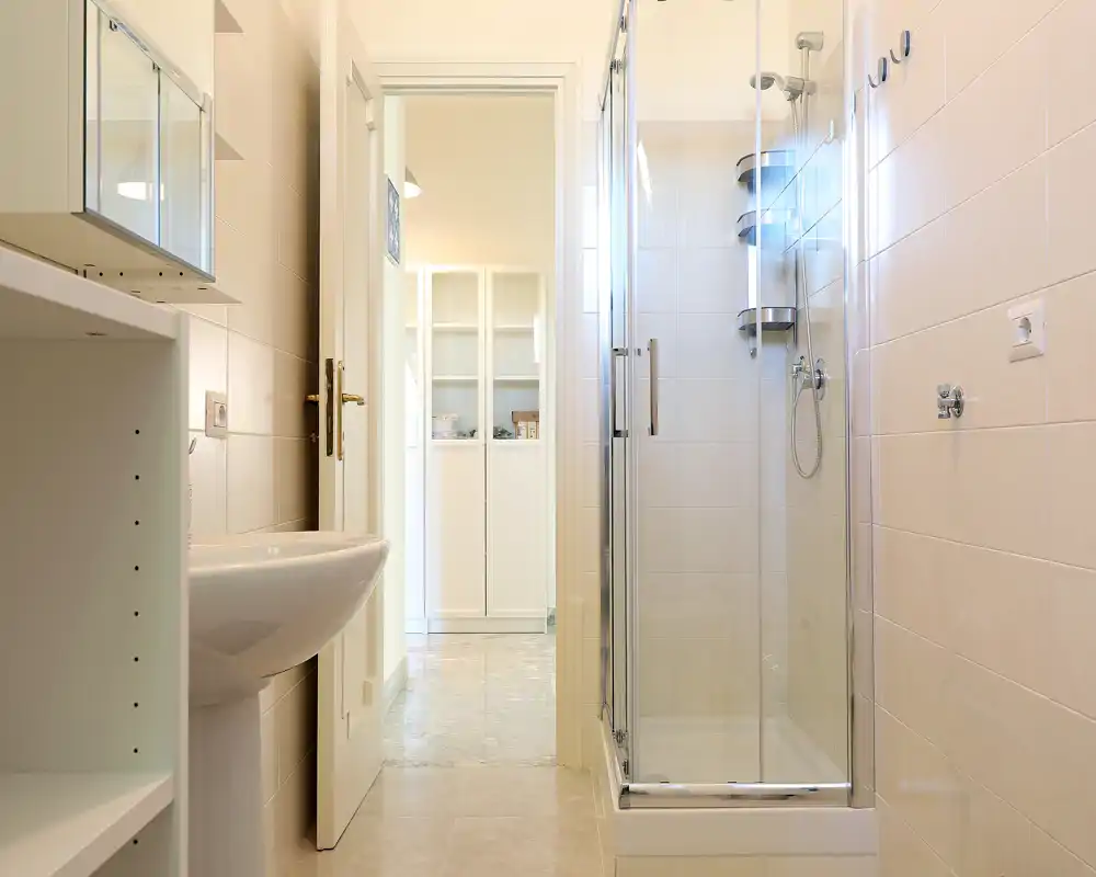 Bright, modern bathroom with a glass-enclosed shower, pedestal sink and neutral tiles—clean and well lit.