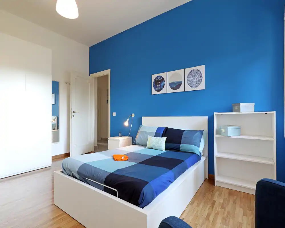 Dormitorio moderno y luminoso con pared azul, muebles blancos y cama doble bien hecha con ropa de cama geométrica — ideal para anuncios de alquiler.