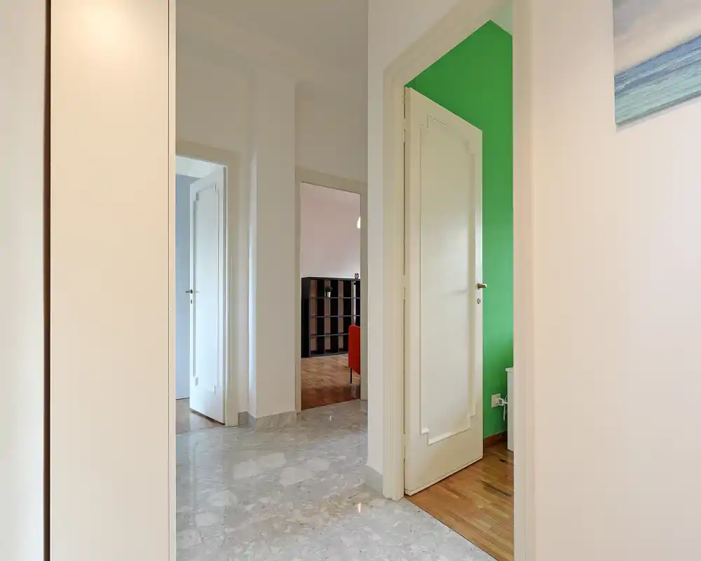 Entrada/pasillo luminoso con suelo de mármol, varias puertas abiertas que conducen a las habitaciones contiguas y paredes blancas limpias—un espacio de paso acogedor.