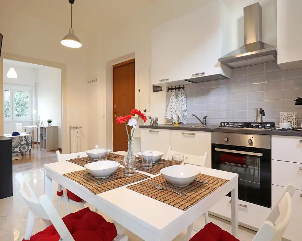 Área de comedor abierta y bien decorada con mesa puesta para cuatro, cocina moderna y luz brillante y aireada — ideal para comidas acogedoras.