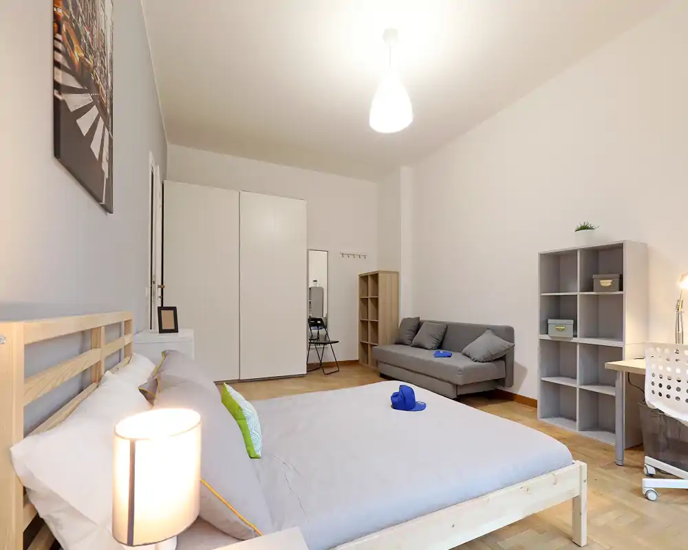 Bright, modern bedroom with a large wooden bed, bedside lamp and a small sofa. Neutral tones, tidy styling and wardrobe storage ideal for rental listings.