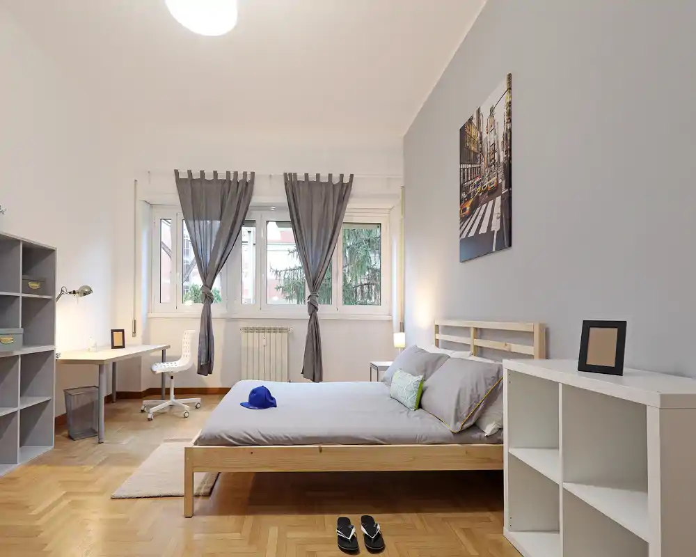 Bright, modern bedroom with a wooden platform bed, large window with tied-back curtains and a workspace corner; calm grey and natural-wood palette creates a relaxed atmosphere ideal for rental listings.