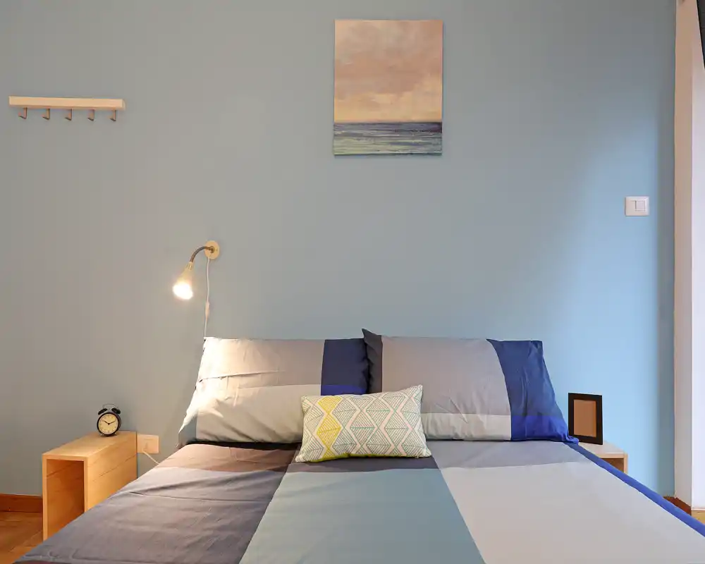 Fresh, well-lit bedroom with a double bed dressed in coordinated linens, a bedside lamp and simple wall art — bright and inviting for travelers.