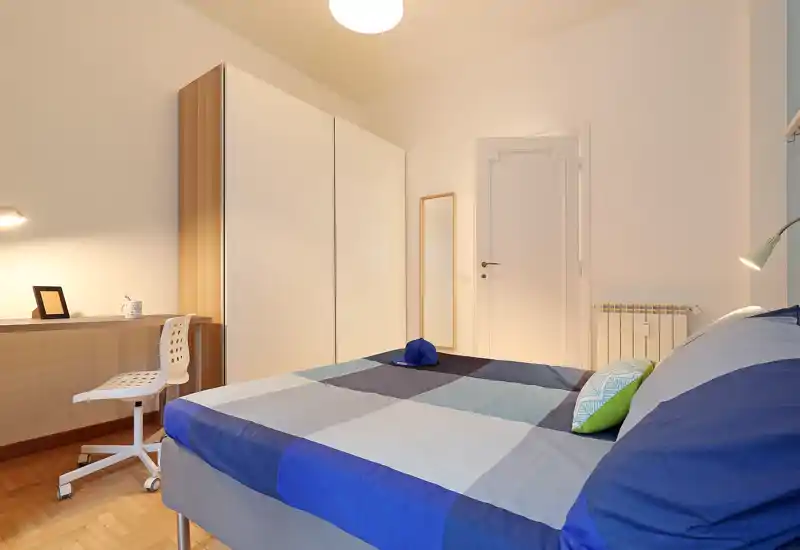 Bright, well-staged bedroom with a blue-check bedspread, wardrobe and study desk. Clean lines and warm lighting create a welcoming space ideal for short-term rentals.