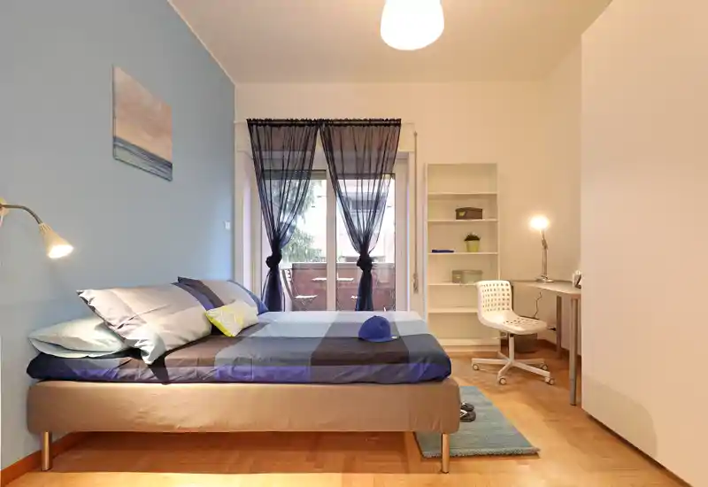 Bright, well-staged bedroom with a double bed, bedside lamp and a desk by the window. Soft blue accent wall and coordinated linens create a calm, welcoming atmosphere for short-term rentals.