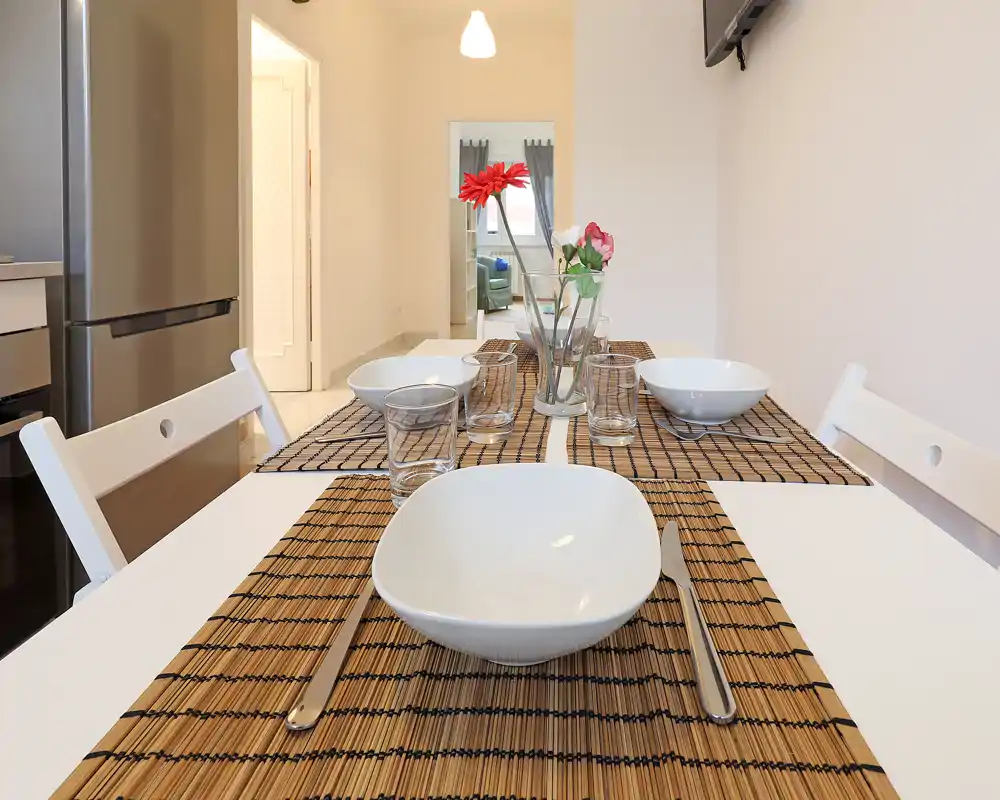 Bright, well-staged dining area with a set table, simple white chairs and decorative flowers—ideal for showcasing mealtime and apartment layout.