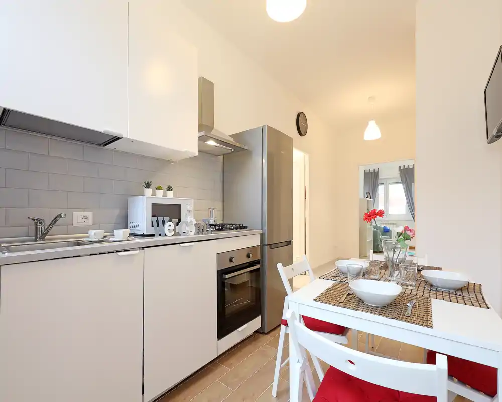 Modern open kitchenette with built-in oven, stainless fridge and a small dining table set for four; bright, clean and well-styled for short-term rentals.