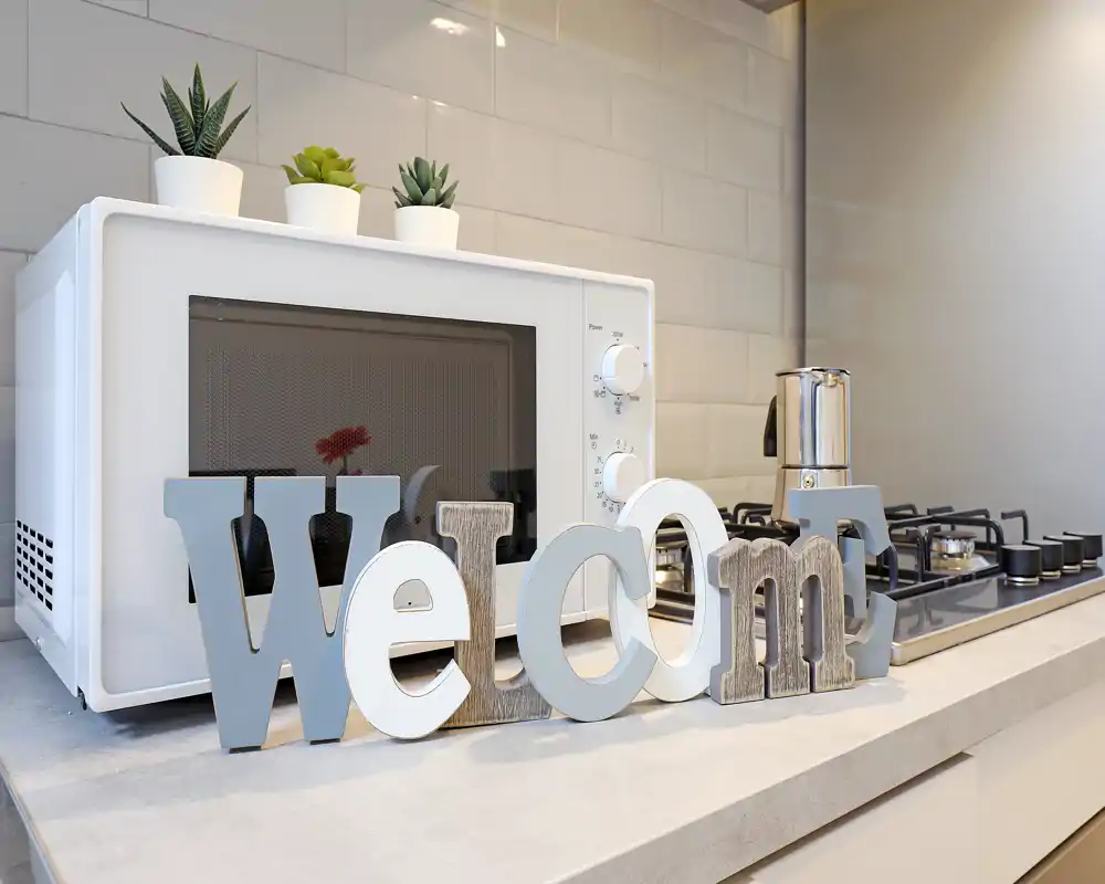 Modern kitchen countertop with a microwave, gas hob and decorative wooden letters; small potted succulents add a fresh accent.