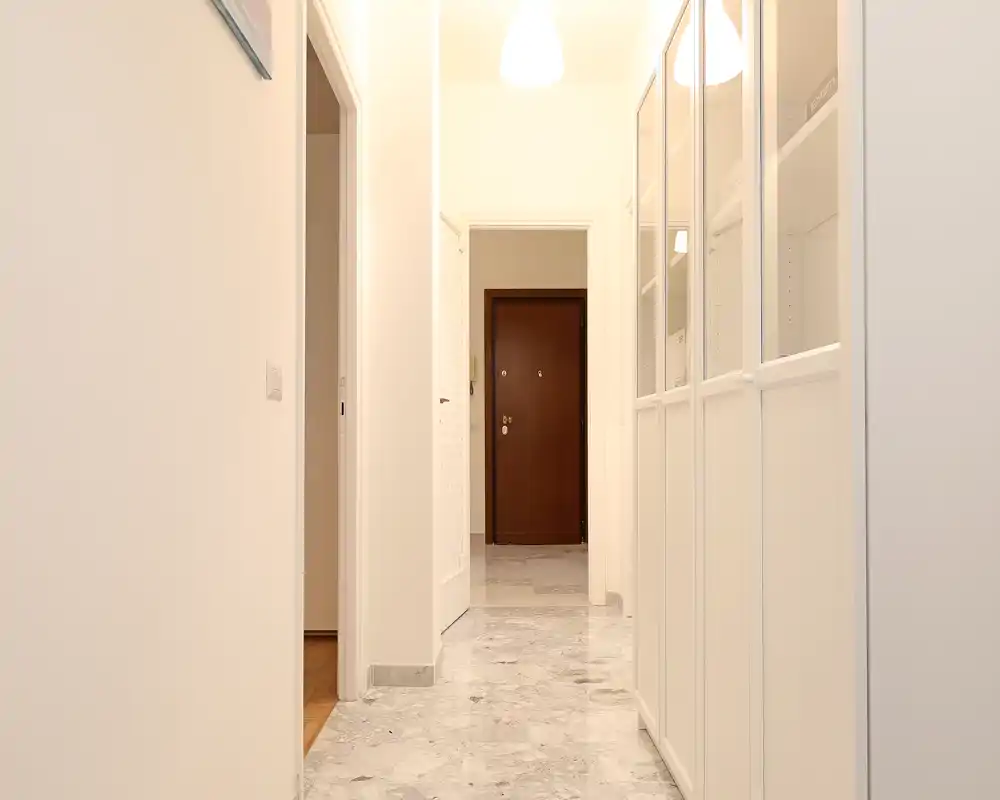 Bright, clean entrance hallway with marble floor and built-in storage cabinets, leading to a solid wood front door; well lit and minimal design suitable for a welcoming entry.