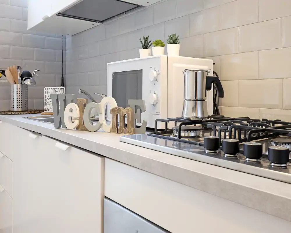 Modern, bright kitchen countertop with a gas hob, microwave, small plants and decorative 'welcome' letters — neat styling ideal for rental photos.